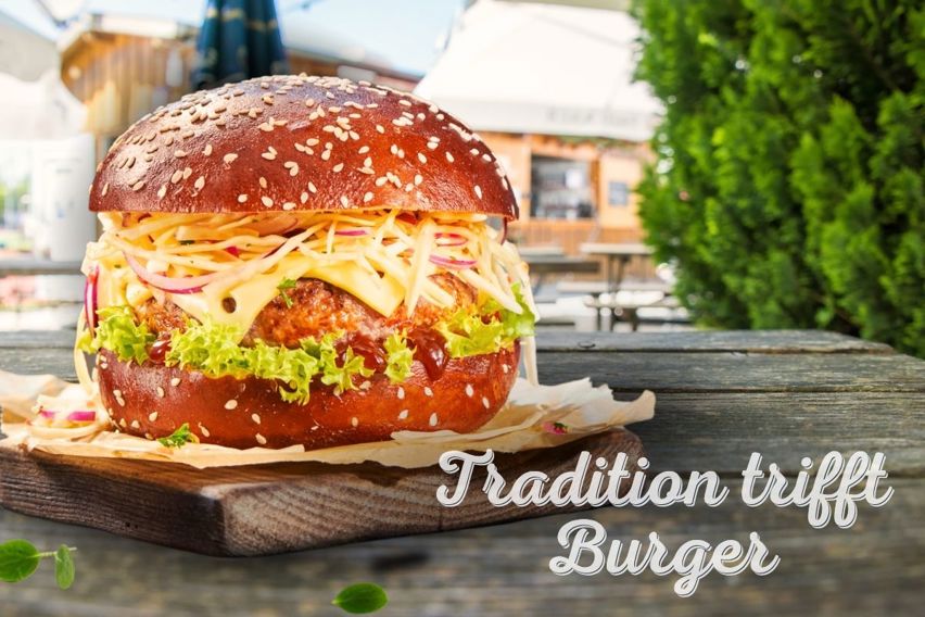 Aufgeschnittener Laugen Burger mit Patty, würzigem Käse und frischem Krautsalat, frontale Ansicht auf Burger mit Holzbrett
